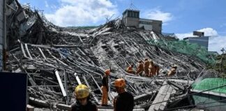 Rescue workers survey collapsed building debris