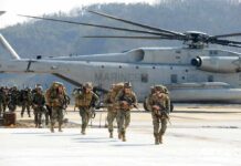 Soldiers disembark and walk past a large military helicopter
