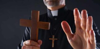 Clergyman holding wooden cross with hand raised