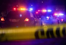 Police cars with flashing lights behind yellow caution tape at night