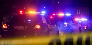 Police cars with flashing lights behind yellow caution tape at night