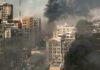 The Safe Zone Paradox in Gaza A cityscape showing damaged buildings and thick smoke rising from the ground