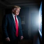Trump’s Russia Plan Meets China’s Resistance A man in a suit and red tie watching a television screen in a dimly lit room