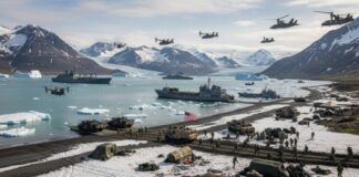 Military personnel and equipment on a snowy beach with helicopters flying overhead
