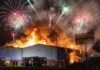A large building engulfed in flames with fireworks in the sky