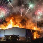A large building engulfed in flames with fireworks in the sky