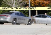Sheriff's line tape blocking a street with police cars behind
