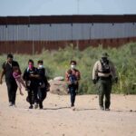 Group walking on a dusty path near a tall border fence