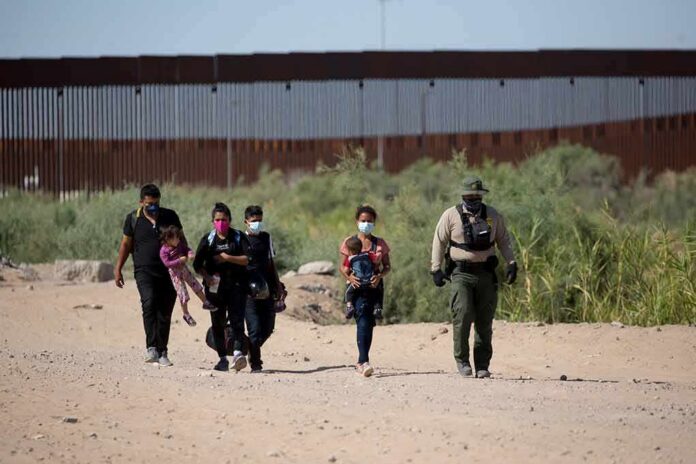 shutterstock_1973414843 Group walking on a dusty path near a tall border fence