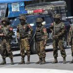 Soldiers in camouflage gear stand in a line on a city street