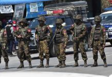 Soldiers in camouflage gear stand in a line on a city street