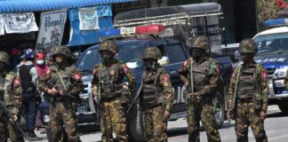 Soldiers in camouflage gear stand in a line on a city street