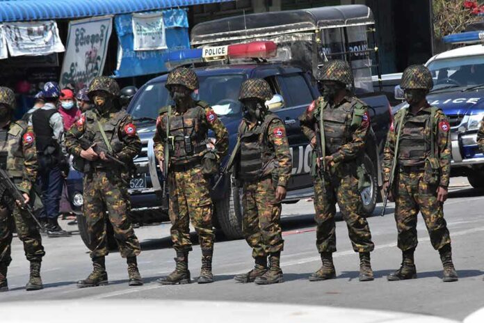 Soldiers in camouflage gear stand in a line on a city street