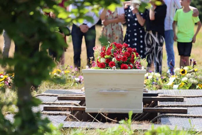 shutterstock_2368329541 White coffin with red flowers at outdoor burial