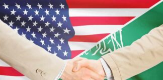 Handshake between two people over U.S. and Saudi flags