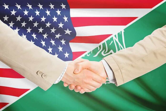Handshake between two people over U.S. and Saudi flags
