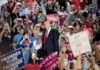 man in suit on stage at crowded rally