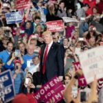 man in suit on stage at crowded rally