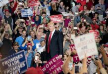 Trump Chokes Tehran’s Cash Lifelines man in suit on stage at crowded rally