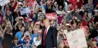 man in suit on stage at crowded rally
