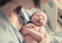 State Fines Doctor—Clinic Carries On newborn baby sleeping in a parent's arms