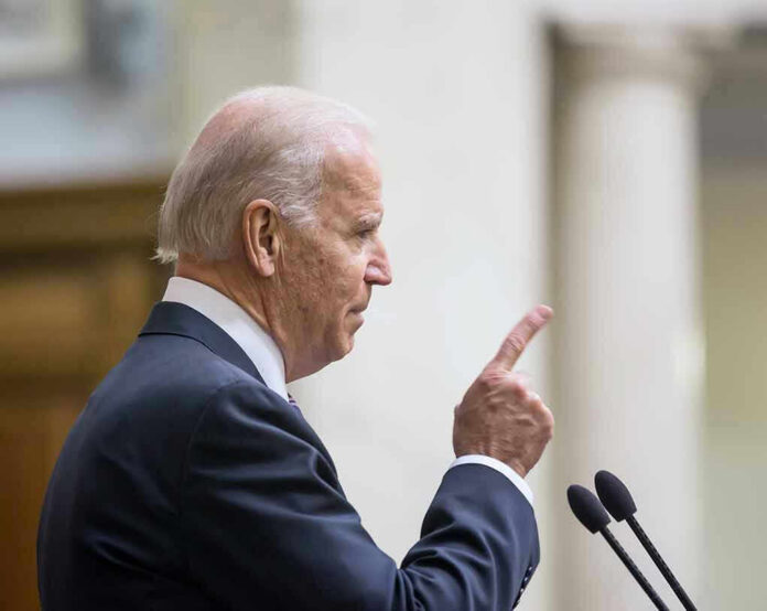 Joe Biden speaking at a podium, pointing upward with his index finger