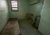 Empty jail cell with bed, barred window, and stainless steel toilet
