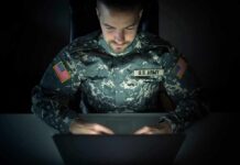 Soldier in camouflage uniform using a laptop in a dark room