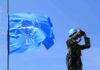 Security Lockdown As Fiery Speeches Loom UN peacekeeper with blue helmet looks through binoculars beside UN flag