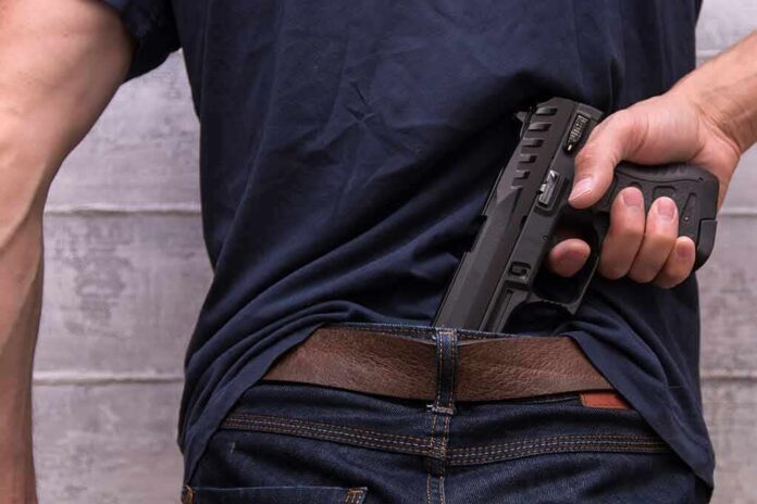 shutterstock_1493432837 Person tucking a handgun into the back waistband