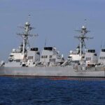 Oil Lifeline Teeters — Wallets Next Three gray naval destroyers docked side by side at a pier