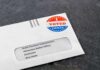 Low-Turnout Shock Tips A Safe Seat Absentee ballot envelope with I Voted sticker on dark surface
