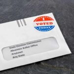 Low-Turnout Shock Tips A Safe Seat Absentee ballot envelope with I Voted sticker on dark surface