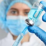 Healthcare worker drawing blue liquid from vial with syringe