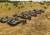 Rows of military tanks with soldiers assembled on a dry field