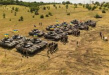Rows of military tanks with soldiers assembled on a dry field