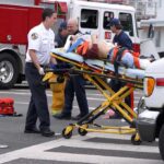 Paramedics wheel an injured person on a stretcher toward an ambulance
