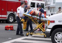 Paramedics wheel an injured person on a stretcher toward an ambulance