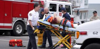 Paramedics wheel an injured person on a stretcher toward an ambulance
