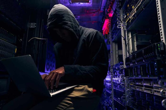 shutterstock_2067215408 Hooded person using a laptop in a dark server room