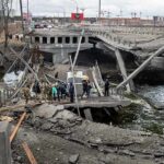 People crossing a destroyed concrete bridge over a river