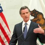 Populist Pivot: Newsom Targets The Ultra-Rich Gavin Newsom speaks at a podium with U.S. and California flags behind him
