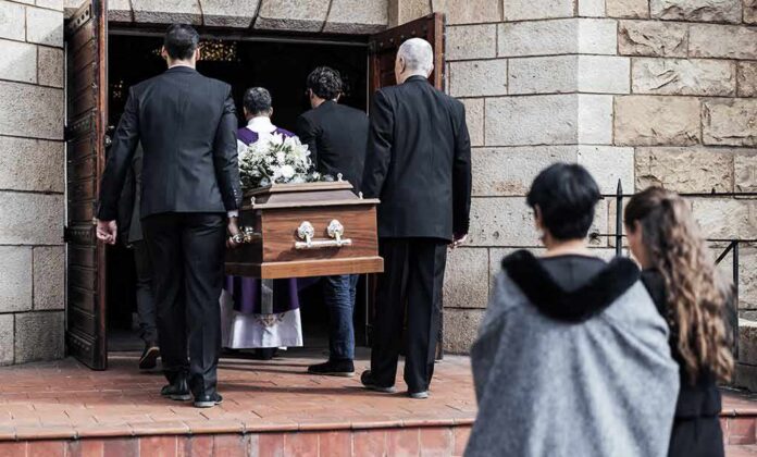 shutterstock_2225085483 Pallbearers carry a casket into a stone church