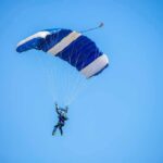 Skydiver descending under a blue parachute