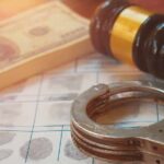 Most Wanted Fraudster Dragged Back — Why Now? Handcuffs on fingerprint form with gavel and cash