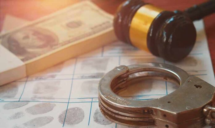 shutterstock_2328292487 Handcuffs on fingerprint form with gavel and cash