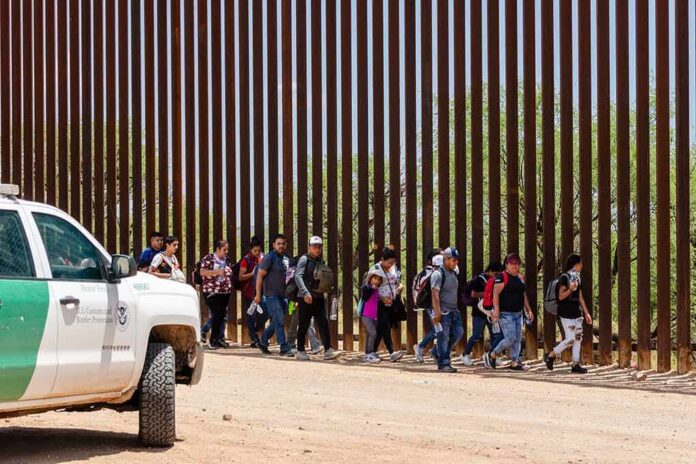 shutterstock_2333258557-1 Group of people walking along a tall border fence beside a patrol vehicle