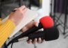 Country Fans Clash Over Late-Night Jokes Journalist holding two microphones while writing in a notebook