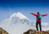 Hiker with arms raised facing snowy mountain peak