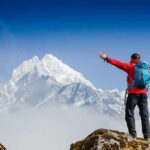 500-Foot Mountain Slide Leads To Overnight Crawl Hiker with arms raised facing snowy mountain peak
